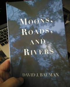 Cover image of poetry chapbook Moons, Roads, and Rivers by David J. Bauman. Dark trees, midnight blue and moonlight white lettering serif font