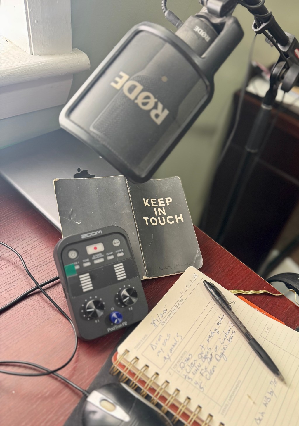 An image from my desk top with journals (one cover says "Keep in Touch") iPad, microphone, and zoom, two-track podcast recorder
