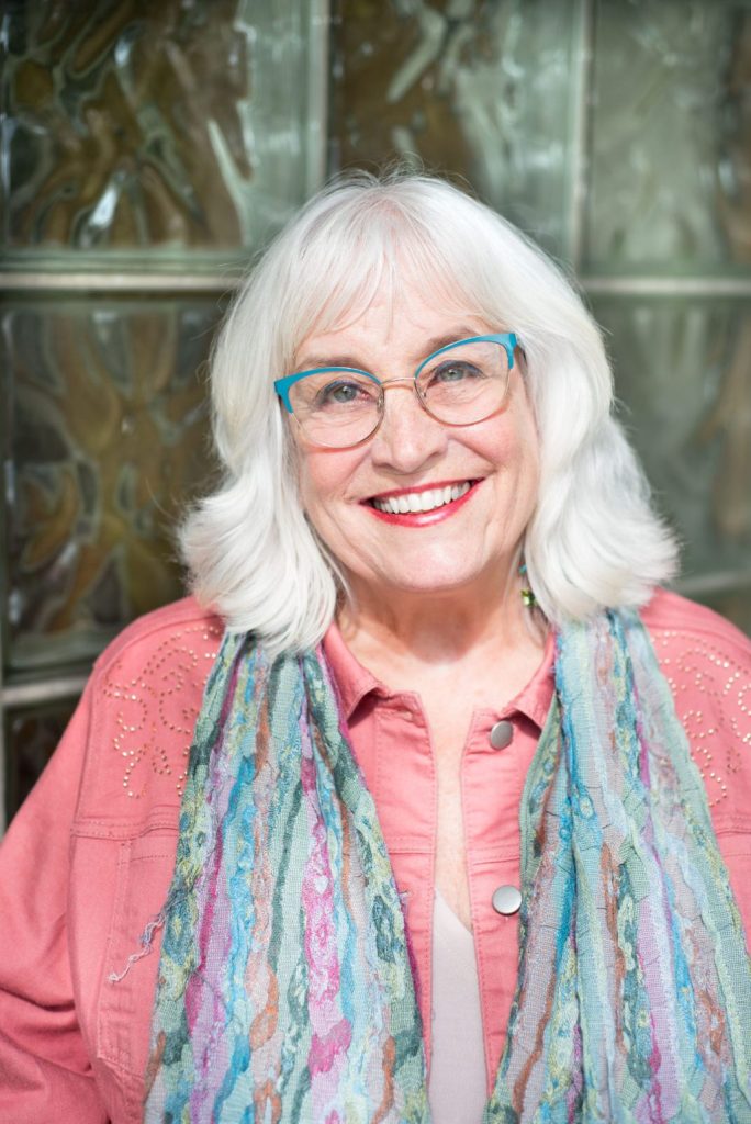 Poet Judith Soenberger, smiling, dressed in pink, some might call i salmon, with a colorful scarf.